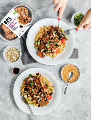 Hands cutting into whole aubergine with orzo salad